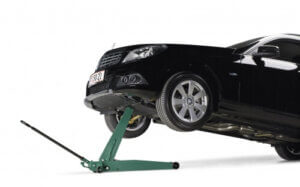 A black car is lifted on one side by a green floor jack, set against a plain white background.