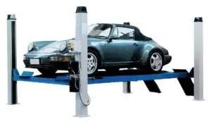 A dark-colored Porsche convertible is elevated on a blue and grey car lift, set against a plain, unadorned white background.