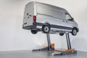 A van is elevated on a vehicle lift inside a bright, nondescript space.