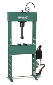 A green hydraulic press with a "OM-PAC" logo, featuring a pressure gauge and a foot pedal, stands idle in a clean, isolated space.