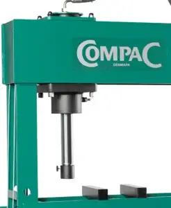 Hydraulic press with the brand name "COMPAC Denmark" on its frame, situated in a workshop environment.