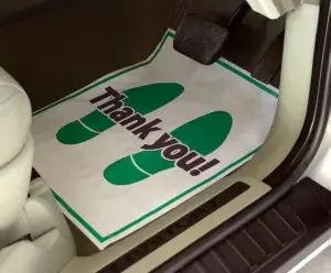 A plastic bag with green footprints and the words "Thank you!" hangs in a car interior, suggesting recent shopping or service completion.