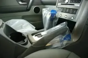 A car's center console and passenger seat covered with clear plastic, likely indicating a newly detailed or sold vehicle interior.