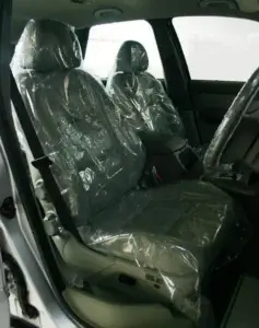 Vehicle interior with seats covered in transparent plastic, indicating either newness or protection, with front and rear seats visible.