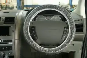 A car steering wheel is covered in plastic wrap, inside a vehicle's interior, suggesting protection or maintenance work.